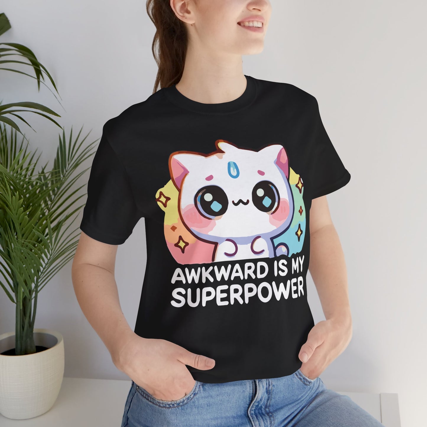 Black t-shirt worn by a smiling woman, featuring a large pastel-colored kawaii cat with sparkles and the phrase "Awkward Is My Superpower" in bold white text.