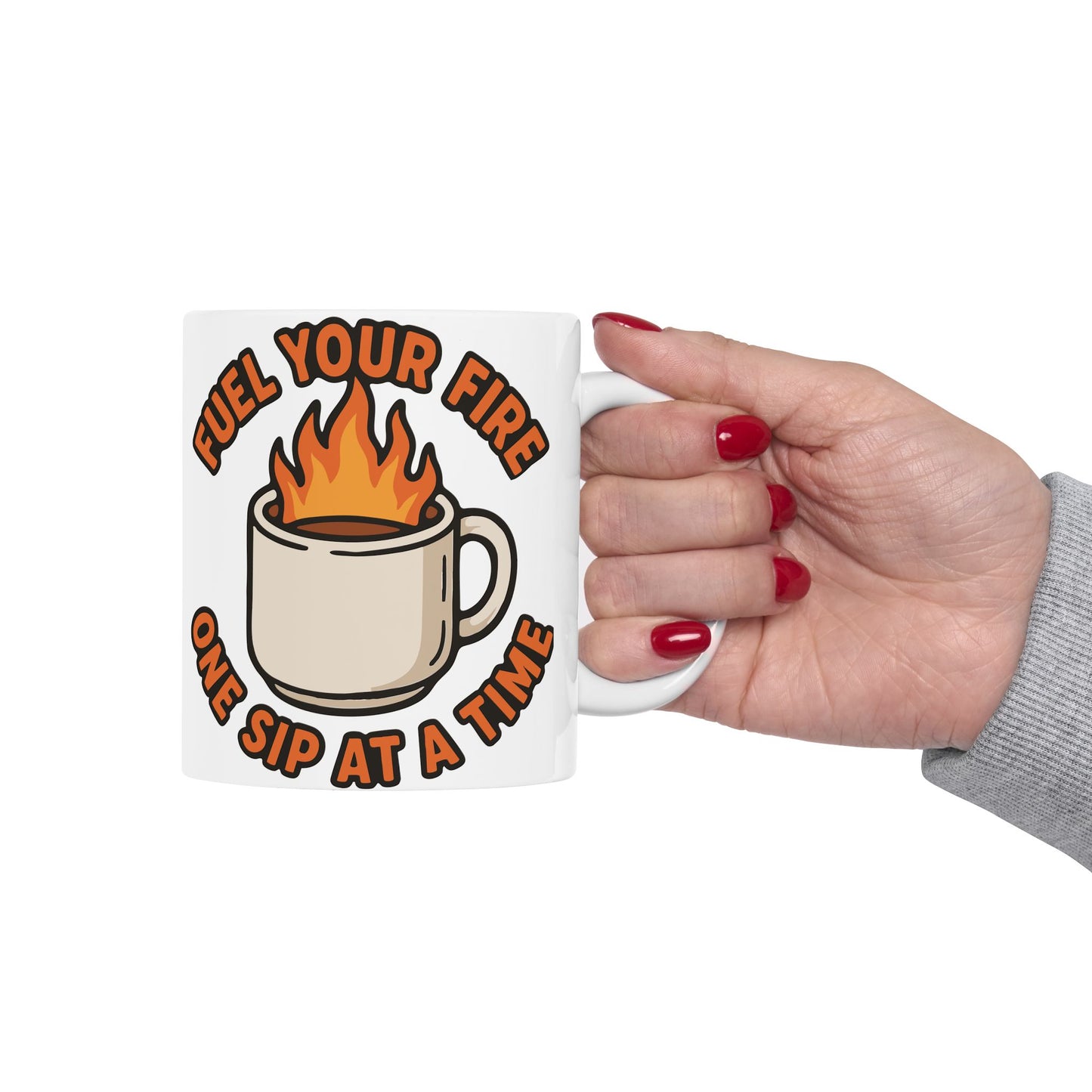 White ceramic mug held in hand, featuring a flaming coffee cup illustration and the motivational quote "Fuel Your Fire One Sip at a Time" in bold orange text.