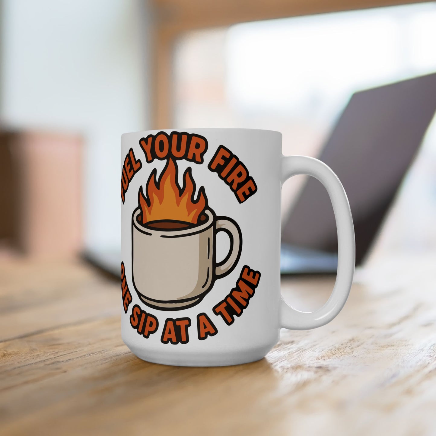 White ceramic mug held in hand, featuring a flaming coffee cup illustration and the motivational quote "Fuel Your Fire One Sip at a Time" in bold orange text.