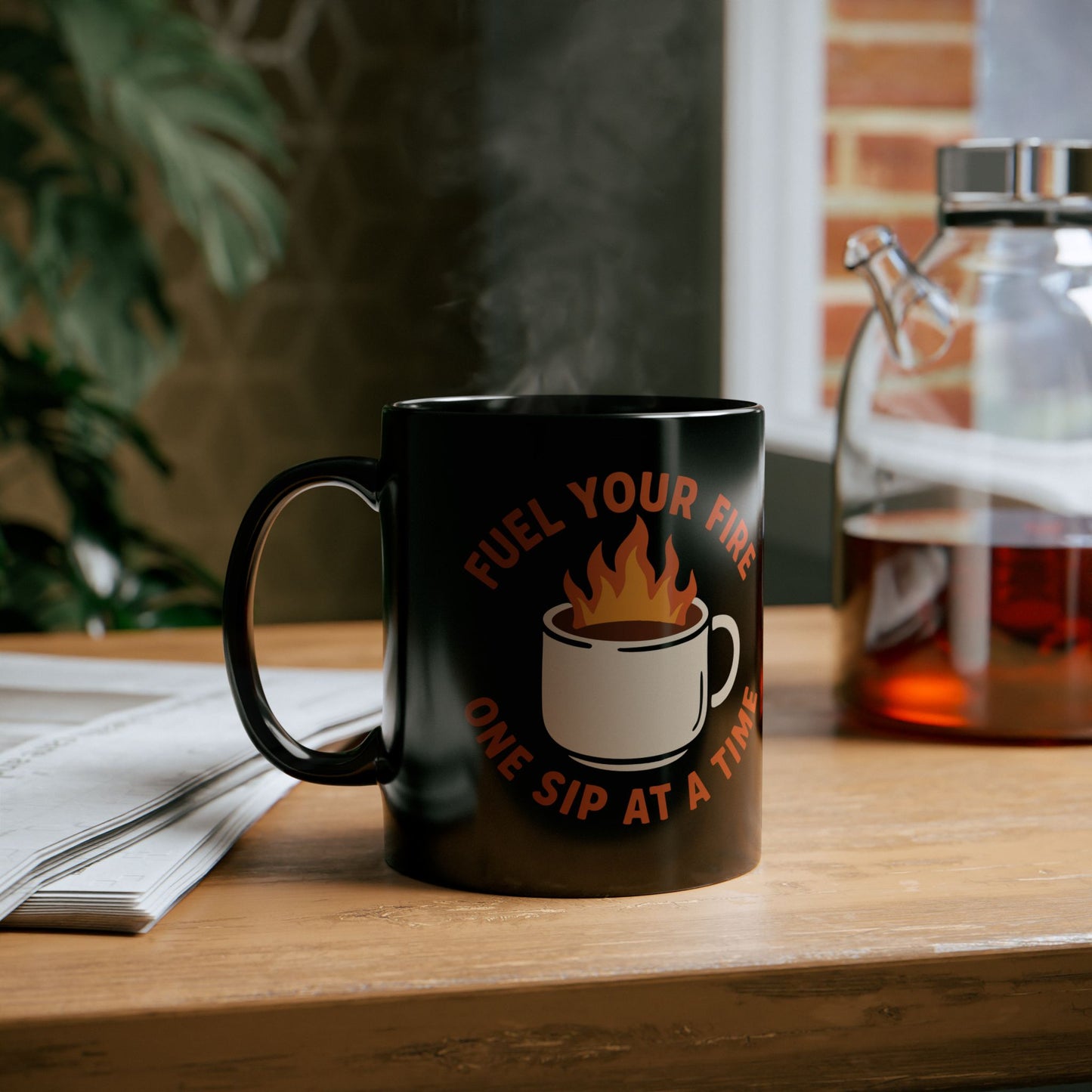Black coffee mug with a bold design of a flaming cup and the motivational phrase "Fuel Your Fire One Sip at a Time" in red-orange text.

