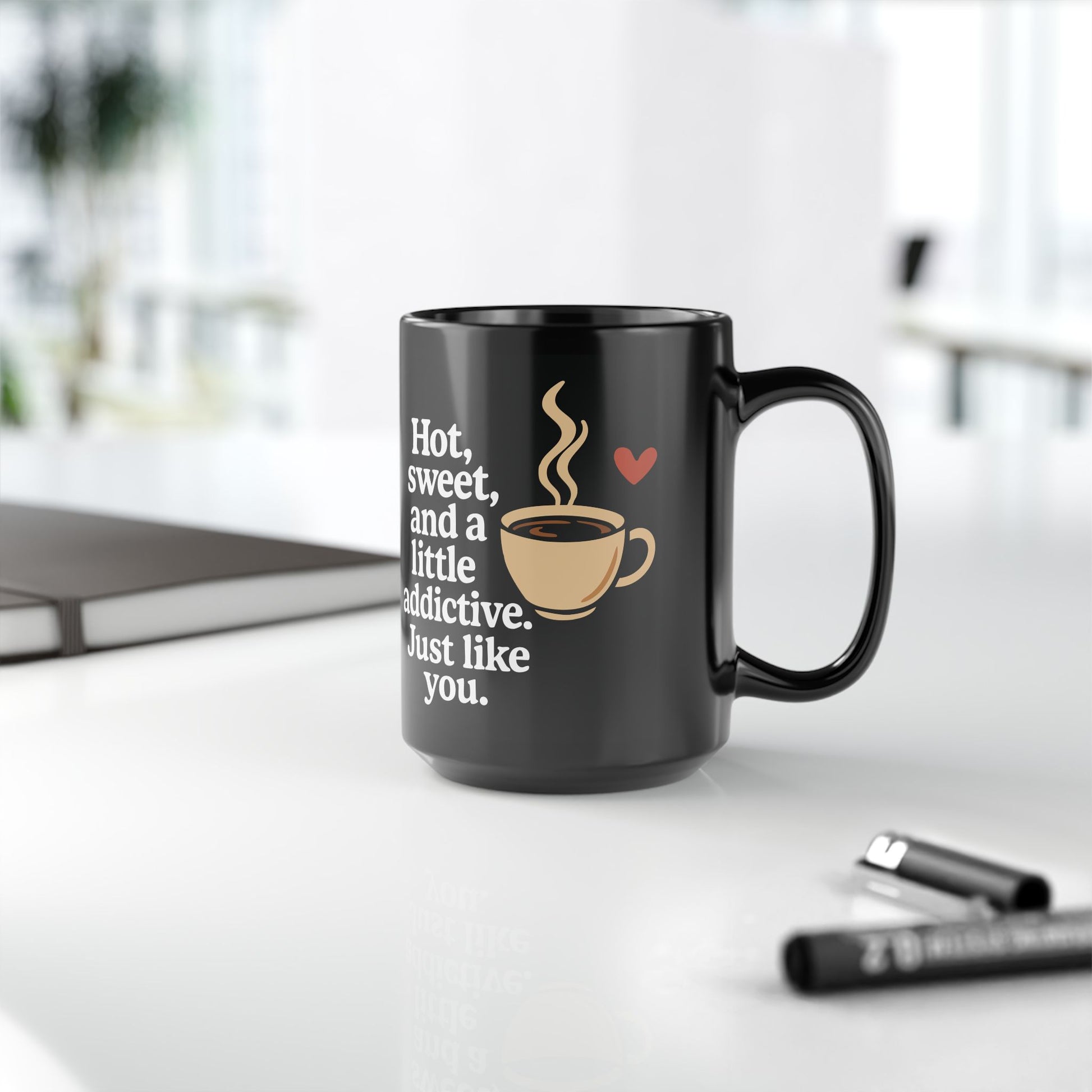 Black ceramic coffee mug with a printed quote "Hot, sweet, and a little addictive. Just like you." alongside a steaming coffee cup and red heart graphic.

