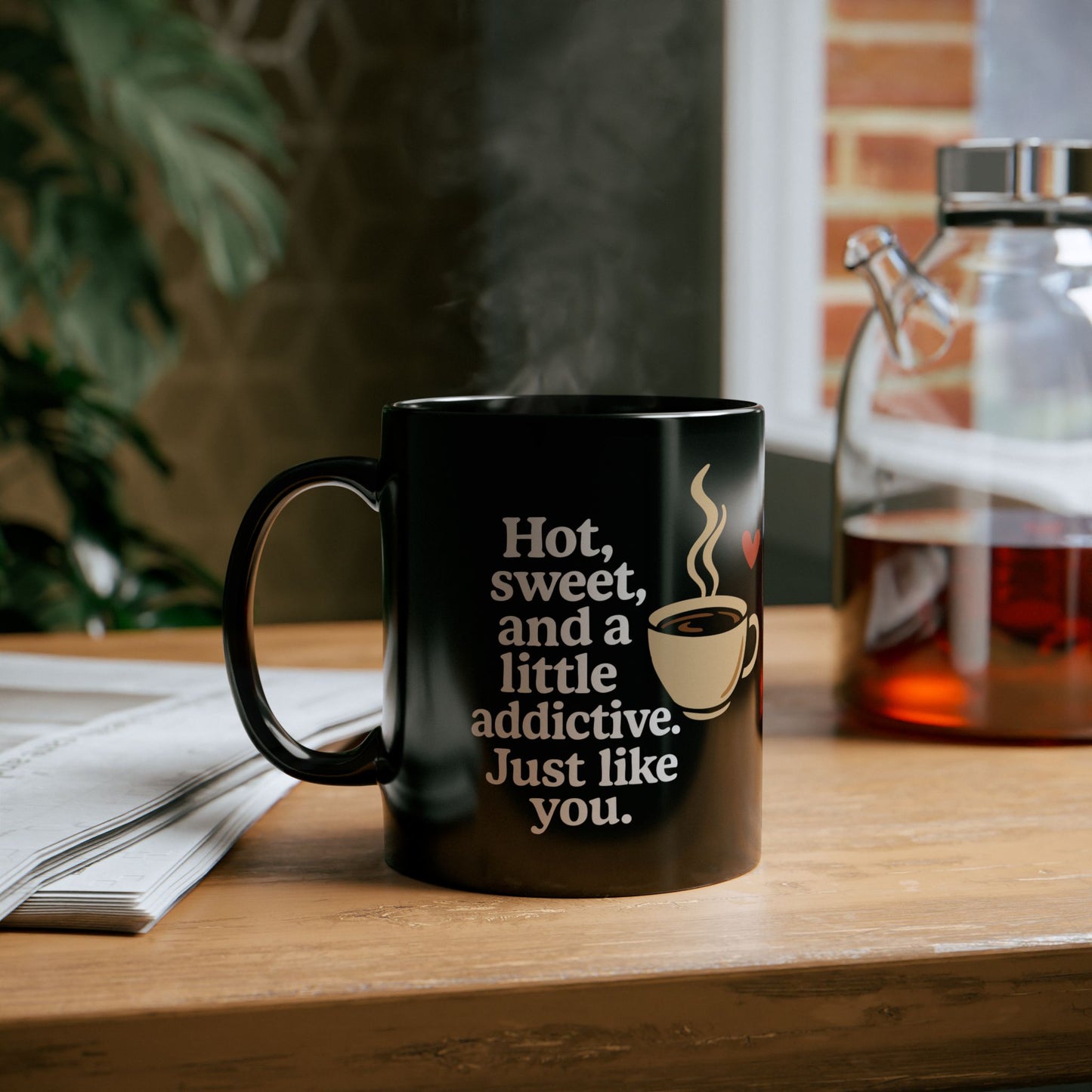 Black ceramic coffee mug with a printed quote "Hot, sweet, and a little addictive. Just like you." alongside a steaming coffee cup and red heart graphic.

