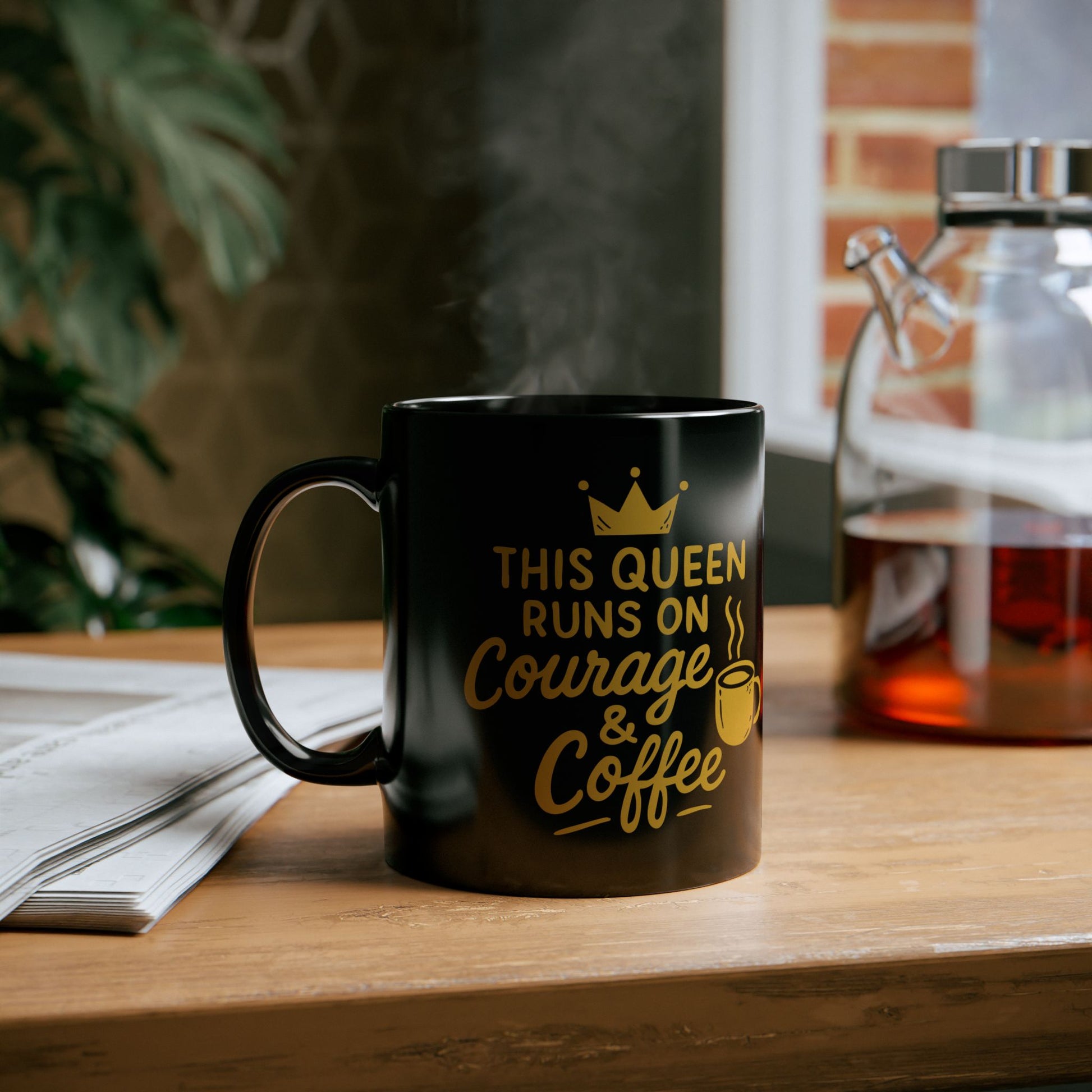 Black ceramic coffee mug with the motivational quote "This Queen Runs on Courage & Coffee" in gold lettering with a crown and steaming coffee cup graphic.
